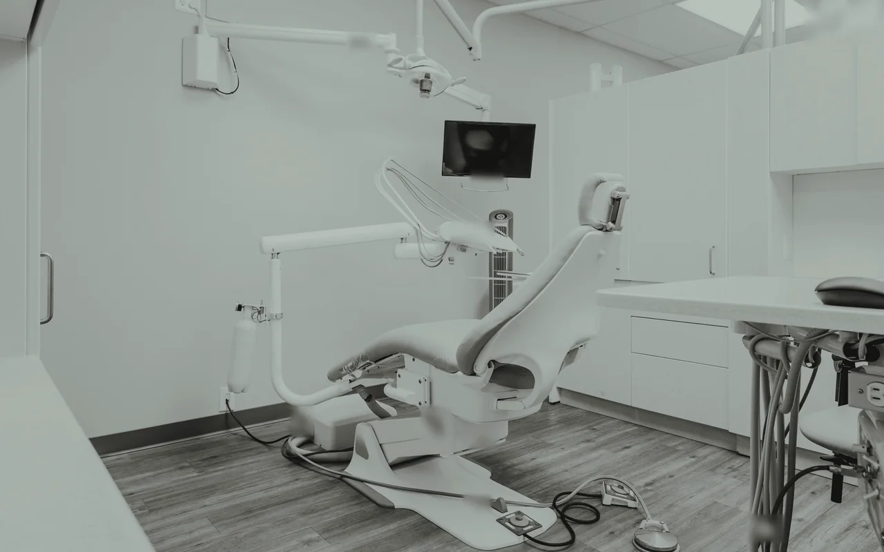 An empty dental treatment room with a chair and a screen.