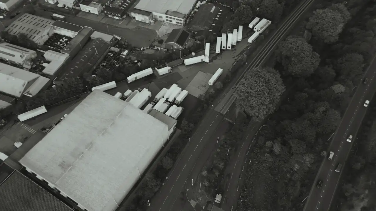 Trucks move around a depot and a warehouse, seen from the air.